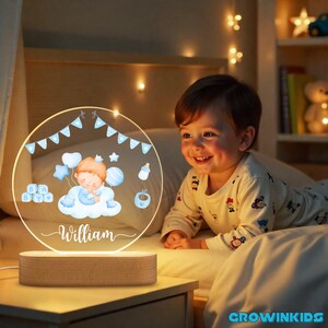 May include: A personalized night light with a wooden base and a circular acrylic design. The design features a baby on a cloud with balloons, stars, and the name "William" in script. The light emits a warm glow.