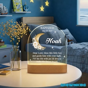 May include: A white acrylic night light with a crescent moon and floral design. The light has a wooden base and a message that reads "BAPTIZED May 25, 2025 Noah Dear Lord, bless this little boy and guide him with your light. Fill his life with joy & love to make his future bright."