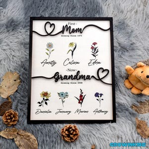 May include: Black wooden sign with a heart design and the text "First-Mom Growing Since 1973" and "Grandma Growing Since 2008". The sign features a floral design with names below each flower.
