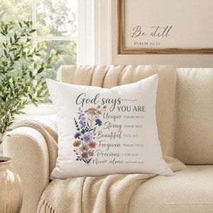 May include: A white square throw pillow featuring a colorful floral illustration on the left side and black text that reads: God says YOU ARE Unique PSALM 139:13, Strong PSALM 18:35, Beautiful ECCL 3:11, Forgiven PSALM 103:12, Precious 1 COR 6:20, Never alone MATTHEW 28:20.