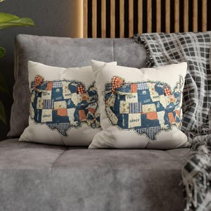 May include: Two decorative throw pillows with a patchwork design in the shape of the United States. The pillows feature a cream background with blue, red, and white fabric patches. The words "Faith," "Hope," and "Grace" are printed on the pillows.