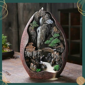 May include: A brown ceramic incense burner shaped like a mountain with a waterfall flowing down the side. The burner features a small house, a bridge, and trees. Smoke flows from the top of the burner, creating the illusion of clouds.