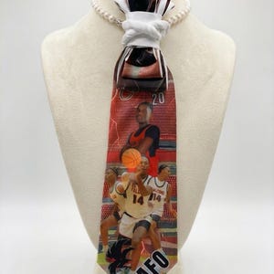 May include: A basketball-themed necktie featuring images of players in action, with the word "NAFO" visible. The tie has a red background with a lightning bolt design and is displayed on a mannequin.