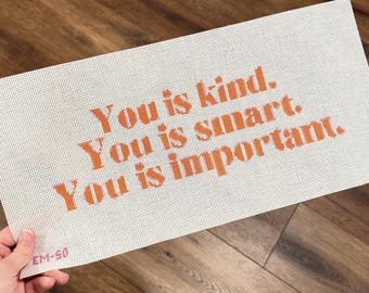 May include: A white needlepoint canvas featuring the orange text "You is kind. You is smart. You is important." The canvas has a grid pattern and includes the small red text "EM-50" in the bottom left corner.
