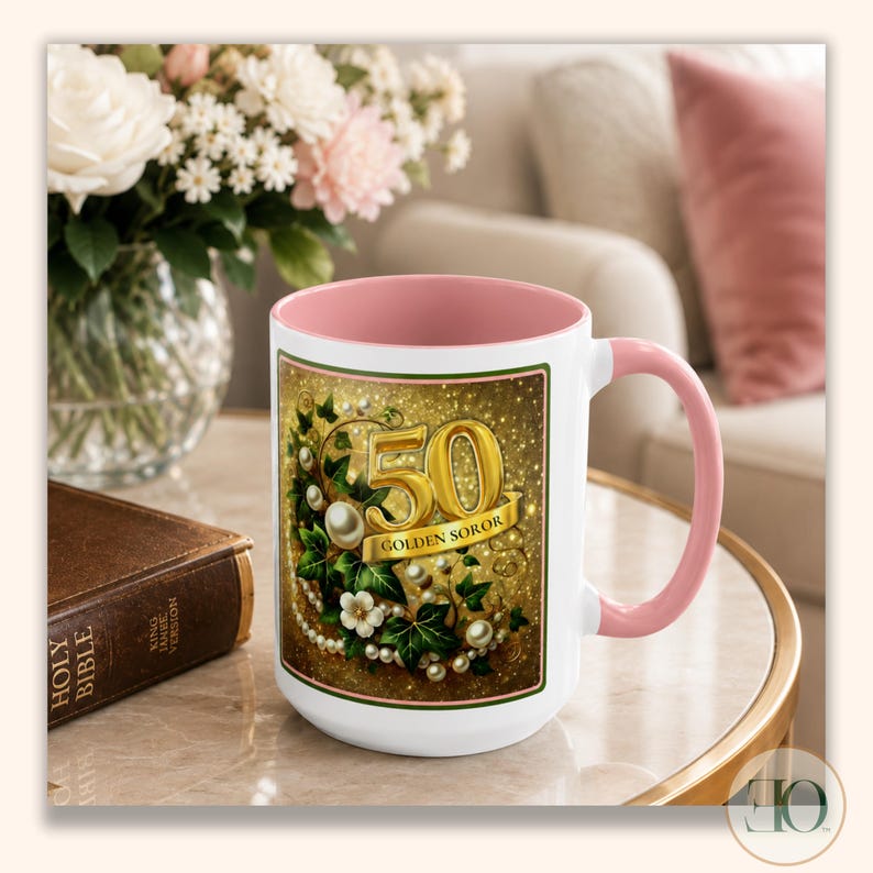 May include: A white ceramic mug with a soft pink interior and handle. The exterior features a rectangular graphic with a gold number 50, the text GOLDEN SOROR, green ivy leaves, white flowers, and strings of white pearls on a gold glitter background.