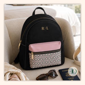 May include: A black backpack featuring a top handle, gold-tone zippers, and the gold-lettered monogram R L. The front pocket has a solid pink upper section and a lower section with a repeating green and pink geometric diamond pattern.
