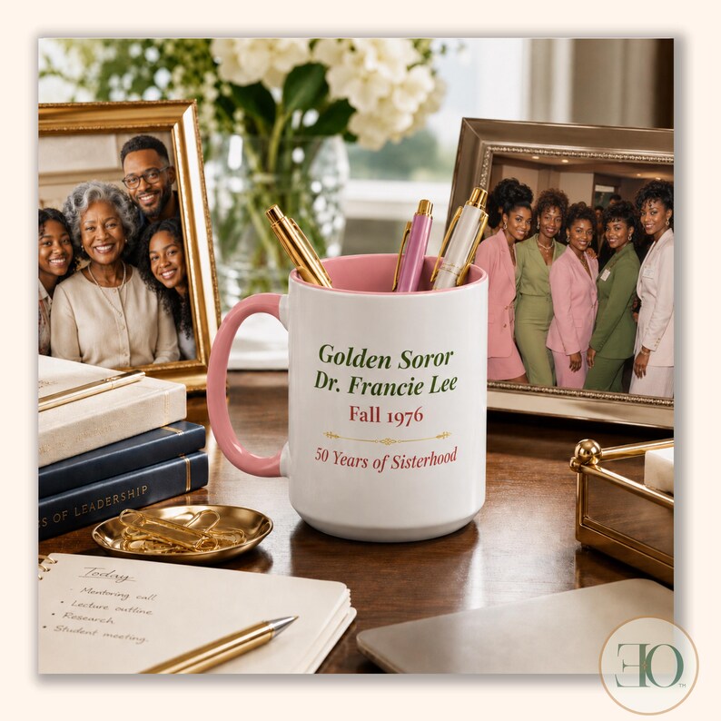 May include: A white ceramic mug with a pink handle and interior, featuring the text Golden Soror Dr. Francie Lee, Fall 1976, and 50 Years of Sisterhood in green and red lettering. The mug contains three pens and sits on a desk with office supplies.