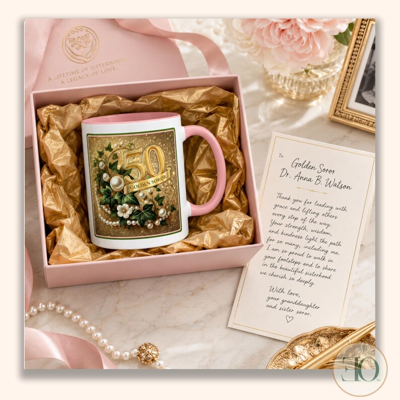 May include: A white ceramic mug with a pink handle and interior, featuring a gold-toned graphic with the number 50, ivy leaves, and pearls. The mug is nestled in a pink gift box with gold tissue paper, accompanied by a printed note to Dr. Anna B. Watson.