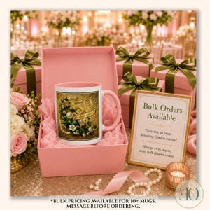 May include: A pink ceramic mug with a graphic featuring the number 50, the text GOLDEN SOROR, pearls, and green leaves, nestled in a pink gift box. A sign nearby reads Bulk Orders Available, Planning an event honoring Golden Sorors?