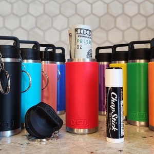 May include: A collection of insulated water bottles in various colors, including purple, gray, black, teal, pink, red, yellow, green, and orange. Each bottle has a black handle and lid. A ChapStick and a rolled-up $100 bill are also visible.