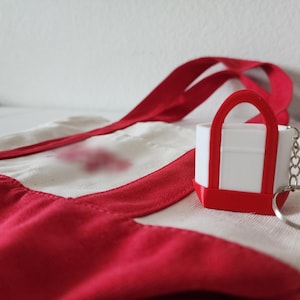 3D printed Trader Joe’s mini canvas tote bag keychain with realistic grocery bag details. Cute miniature keychain replica of the iconic Trader Joe’s shopping tote, perfect for Trader Joe’s lovers and collectors. Unique 3D printed accessory for keys, backpacks, or purses. Eco-friendly, handmade keychain gift for grocery store fans, foodies, or novelty bag charm collectors. Great stocking stuffer or personalized gift idea.