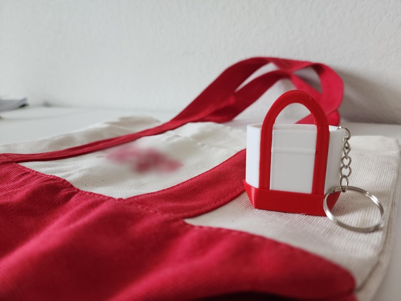 3D printed Trader Joe’s mini canvas tote bag keychain with realistic grocery bag details. Cute miniature keychain replica of the iconic Trader Joe’s shopping tote, perfect for Trader Joe’s lovers and collectors. Unique 3D printed accessory for keys, backpacks, or purses. Eco-friendly, handmade keychain gift for grocery store fans, foodies, or novelty bag charm collectors. Great stocking stuffer or personalized gift idea.