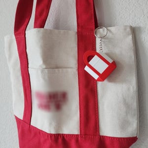 3D printed Trader Joe’s mini canvas tote bag keychain with realistic grocery bag details. Cute miniature keychain replica of the iconic Trader Joe’s shopping tote, perfect for Trader Joe’s lovers and collectors. Unique 3D printed accessory for keys, backpacks, or purses. Eco-friendly, handmade keychain gift for grocery store fans, foodies, or novelty bag charm collectors. Great stocking stuffer or personalized gift idea.