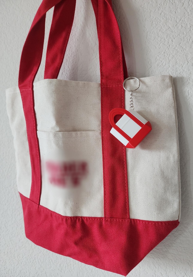 3D printed Trader Joe’s mini canvas tote bag keychain with realistic grocery bag details. Cute miniature keychain replica of the iconic Trader Joe’s shopping tote, perfect for Trader Joe’s lovers and collectors. Unique 3D printed accessory for keys, backpacks, or purses. Eco-friendly, handmade keychain gift for grocery store fans, foodies, or novelty bag charm collectors. Great stocking stuffer or personalized gift idea.