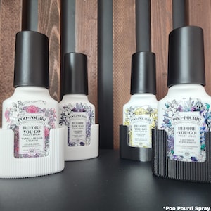 Puede incluir: Cuatro botellas blancas de spray de inodoro "Poo-Pourri Before You Go" con tapas negras, cada una en un soporte diferente. Las botellas tienen diseños florales y el texto "Before You Go". Los soportes son blancos y negros.