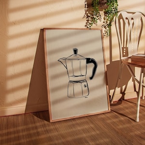 Puede incluir: Un dibujo en blanco y negro de una cafetera italiana tradicional, o cafetera Moka, sobre un fondo beige. El dibujo está enmarcado en un marco de madera marrón claro.