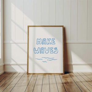 May include: A framed print with a white background and the text "MAKE WAVES" in blue. The text is in a hand-drawn style with wavy lines underneath.