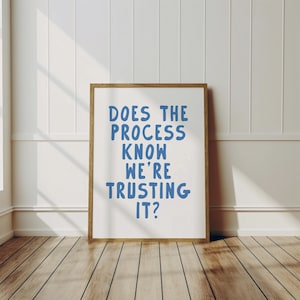 Op de afbeelding: Een ingelijst afdruk met een witte achtergrond en een blauwe inscriptie die luidt "Does the process know we're trusting it?"