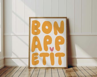 May include: A framed print with the text "BON APPETIT" in yellow letters with a pink heart in the middle of the word "APPETIT". The background is white.