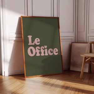 Op de afbeelding: Een ingelijst print met een donkergroene achtergrond en roze tekst die "Le Office" luidt met een klein hartje boven de "e" in "Office".