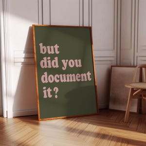 May include: A rectangular wall art print in a wooden frame featuring a dark olive green background with the text "but did you document it?" written in a light pink, rounded, retro-style font. The print is displayed in a vertical orientation.