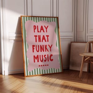 May include: A framed art print with the words "PLAY THAT FUNKY MUSIC" in red on a pink, wavy shape. The background has green and white stripes. The frame is brown, and the print is leaning against a white wall.