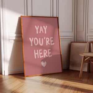 Puede incluir: Un póster enmarcado en rosa con el texto "YAY YOU'RE HERE" en letras blancas y un pequeño corazón rosa en la esquina inferior derecha.