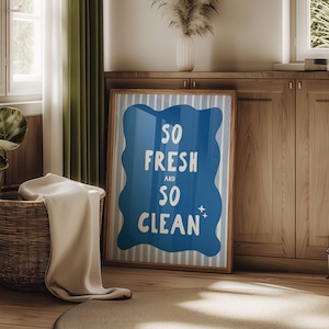 以下が含まれることがあります： 「SO FRESH and SO CLEAN」の文字が白で書かれた、青色の波型のフレームプリント。背景には青と白のストライプがあります。ベージュの毛布が入ったバスケットが前景にあります。