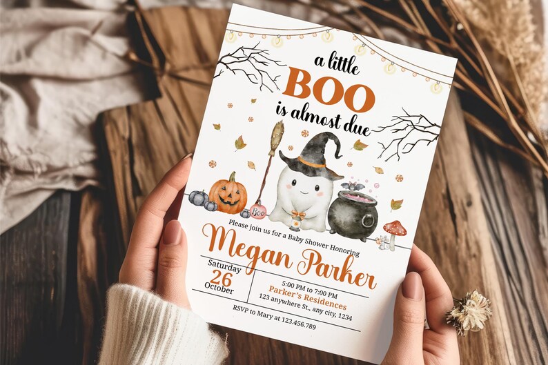 May include: A Halloween-themed baby shower invitation with the text "a little BOO is almost due." The invitation features a ghost wearing a witch hat, a pumpkin, and a cauldron. The invitation is held by a person.