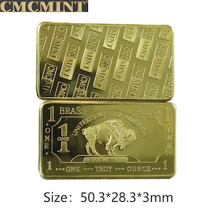 Op de afbeelding: Twee goudkleurige messing bullion bars. Eén bar heeft een herhalend patroon van "CMCMINT" tekst. De andere bar toont een buffelafbeelding, de tekst "United States of America" en "One Troy Ounce". Afmetingen: 5,03 x 2,83 x 0,3 cm.