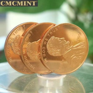 May include: Four gold-coloured coins are displayed, each with a profile and the inscription "IN GOD WE TRUST." The year "2009" is visible on one coin. The coins are arranged in a fan shape, slightly overlapping. The "CMCMINT" logo is in the top left corner.