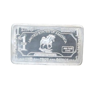 Op de afbeelding: Een rechthoekige zilveren bullion bar met de tekst "UNITED STATES OF AMERICA" en een paardenafbeelding. De bar bevat ook de tekst "ONE TROY OUNCE" en "ZINC".
