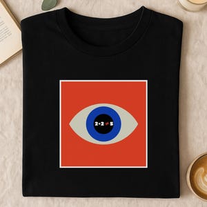 May include: Black t-shirt with a graphic eye design. The eye has a blue iris, a grey eyelid, and the text "2+2≠5" in the centre. The eye is set against a red square with a white border. A modern design.