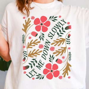 Puede incluir: Camiseta blanca con un diseño floral y el texto "Let me down slowly".
