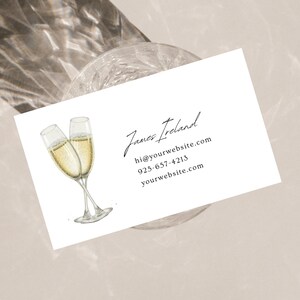May include: A white business card with a black handwritten signature that reads "James Ireland". The card also includes contact information: "hi@yourwebsite.com", "925-657-4213", and "yourwebsite.com". The card features a watercolour illustration of two champagne flutes.