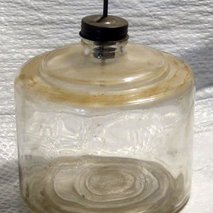 May include: A clear glass bottle with a metal lid and a metal spout. The bottle has a textured surface and is empty.