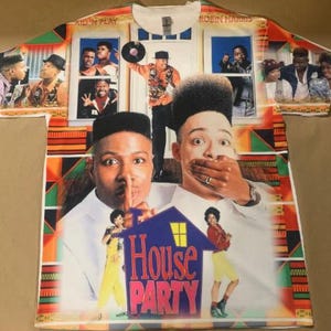 May include: White t-shirt featuring a colorful graphic design with images of the movie "House Party" and the text "House Party". The shirt has a crew neck and short sleeves. The design includes images of actors and the movie title.