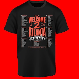 May include: A black short-sleeve t-shirt featuring a graphic print in red and white. The design includes the text "WELCOME 2 ATLANTA" with a crown, a peach icon, a city skyline silhouette, and lists of various city neighborhoods organized by zones.