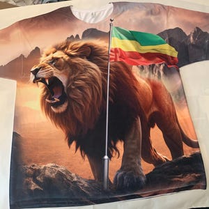 May include: A white t-shirt with a roaring lion and a flag with red, yellow, and green stripes. The lion is standing on a rocky mountain with a sunset in the background.