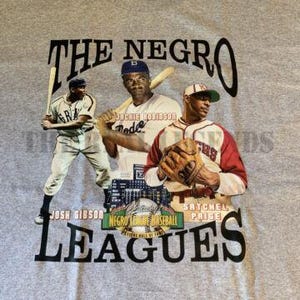 May include: A gray t-shirt with a graphic print of three baseball players. The text "The Negro Leagues" is printed in black at the top of the shirt. The text "Negro League Baseball" is printed in white on a black background at the bottom of the shirt.