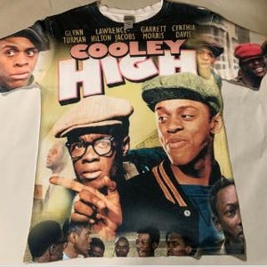 May include: A white t-shirt with a colourful print of the film "Cooley High" featuring the actors Lawrence Hilton Jacobs, Garrett Morris, and Glynn Turman. The shirt has a crew neck and short sleeves.