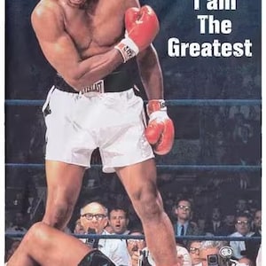 May include: A poster featuring Muhammad Ali standing over a defeated opponent in a boxing ring. Ali, wearing red gloves and white shorts, is shouting. The text "I am The Greatest" is displayed.