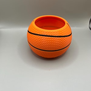 May include: Orange and black basketball-shaped planter with a textured surface.