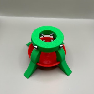 May include: A green and red 3D printed Christmas tree stand with a circular base and three legs.