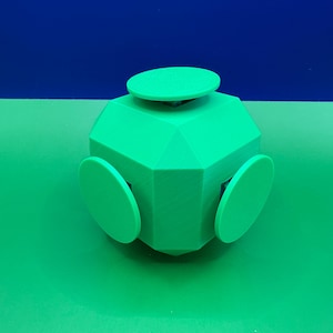May include: A bright green geometric object featuring a central cube-like structure with flat, circular discs attached to each of its visible faces. The object has a smooth, matte finish and a symmetrical design with sharp, defined edges and corners.