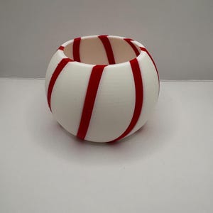 May include: A round, white decorative bowl with red stripes. The stripes are evenly spaced and wrap around the bowl. The bowl has a smooth surface and a wide opening. The bowl is sitting on a white surface.