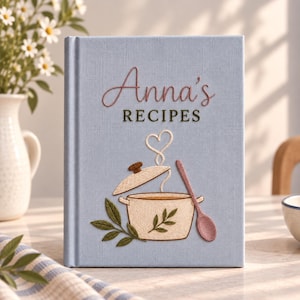 May include: A light blue hardback recipe book featuring embroidered text that reads Anna's RECIPES. The cover displays an embroidered design of a cooking pot with a lid, a wooden spoon, and green leaves, with steam forming a heart shape above.