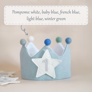 Op de afbeelding: Een lichtblauwe kroon van vilt met een witte viltster en het getal "1" erop geborduurd. De kroon is versierd met pompoenen in wit, babyblauw, Frans blauw, lichtblauw en wintergroen.
