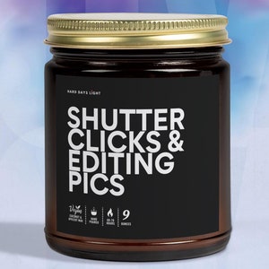 May include: A brown glass candle jar with a gold lid. The label is black with white text that reads "Shutter Clicks & Editing Pics". The candle is vegan, hand-poured, and has a burn time of 60-70 hours. It is 9 ounces.