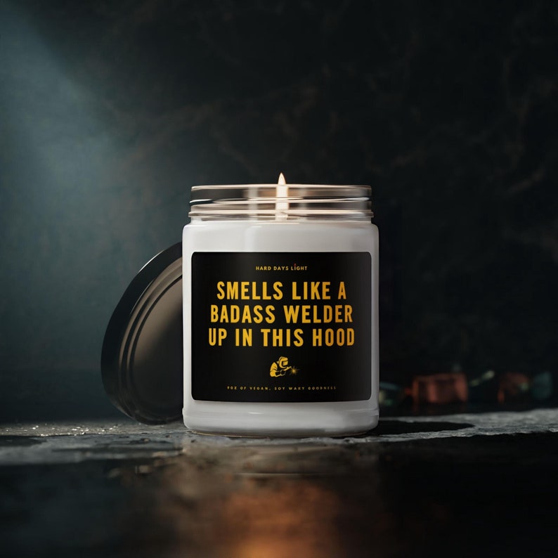This is a 9 ounce white soy wax candle for a Welder.   It says "Smells like a badass welder up in this hood".  The label is black with yellow gold lettering a graphic of a welder in a welding hood.